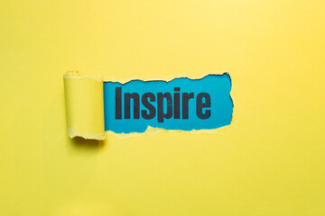 inspire word written with stamp letters, on blue paper seen thru ripped yellow paper
