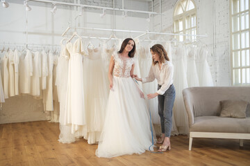 Naklejka premium Skillful dress designer fitting wedding gown to woman in her boutique. Woman making adjustments to bridal gown in fashion designer studio.