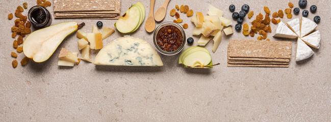 Creative cheese platter. Variety soft and hard cheeses, fruit, jam on beige concrete background....