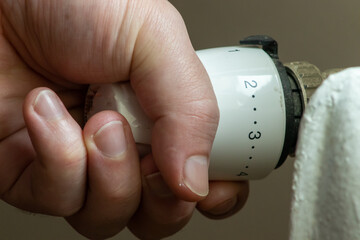Close up hand adjusting heating temperature. Reducing heating cost in crisis. War in Ukraine. Energy crisis. regulating temperature knob concept