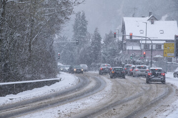 Schneebedeckte Strasse mit Fahrspuren, Fahrzeugen,Ampelanlage und Schneegestöber