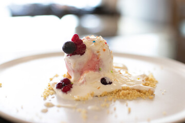 Ice cream with crumble and berry on top. Dessert on white plate.