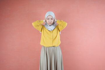 Beautiful Asian woman in yellow shirt and hijab covering ears with hands on brown background 