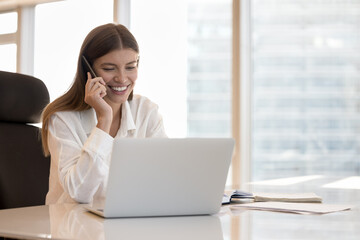 Positive busy young employee girl using digital gadgets at workplace for business communication,...