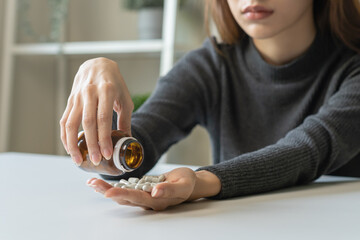 Anti drugs, drug addict, asian young woman hand pour, holding bulk medicine out of pills bottle on table at home, abuse overdose. Sick pain of health, unhealthy people. Suicide depressed or despair.