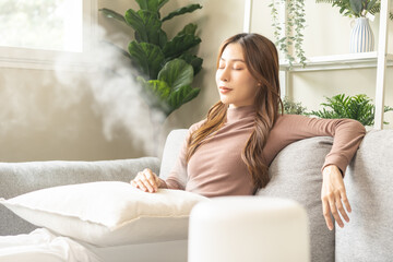 Modern air humidifier during relax or rest, happy asian young woman, girl enjoying aromatherapy steam scent from essential oil diffuser comfortable in living conditions room, apartment at home. - obrazy, fototapety, plakaty