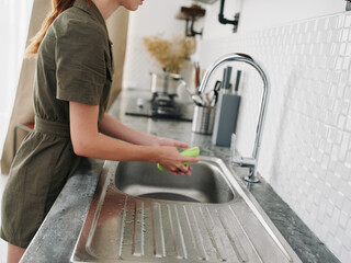 Woman smiling with teeth hands without gloves washes dishes plate with a bubble dishwashing sponge, household chores, no dishwasher, high water consumption. Stylish kitchen design, house cleaning