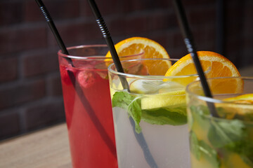 several different drinks on table, lemonade in glass, slice of lemon and straws, dark background, indoors