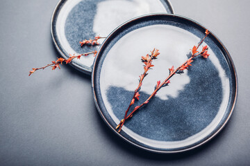 Handmade ceramic plates decorated with spring branches. Close up of blue vintage dishes on grey background. Space