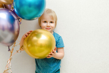 Fototapeta na wymiar Blond cute happy Child kid boy celebrating third birthday with colorful balloons at party,home in front of wall.baby smiling looking at camera.adorable caucasian baby.Festive background decoration