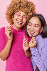 Vertical shot of cheerful women apply makeup use professional lipstick smile broadly stand closely...