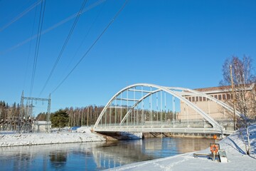 Obraz premium Modern bridge with snow on the ground and river flowing without ice in winter at Ahvenkoski, Pyhtää, Finland.