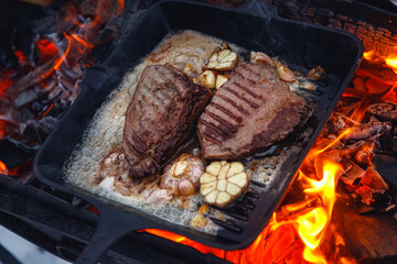 Steak on fire. Cast iron frying pan. Fresh meat. Open fire. Barbecue. Firewood.