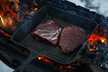 Steak on fire. Cast iron frying pan. Fresh meat. Open fire. Barbecue. Firewood.