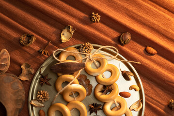  A bunch of bagels lie on a bronze platter, decorated with dried flowers and herbs. On a background of brown corrugated paper