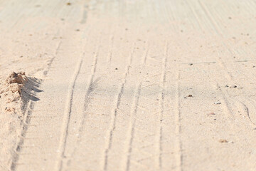 Close-up tire tracks on white sand and a tiny sand hill with shadow. 