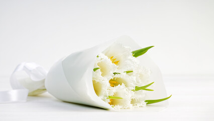 Closeup bouquet of white tulips wrapped in paper on a white wooden table. Copyspace.