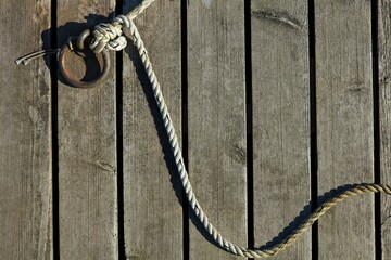 Obraz premium Rope fastened to a metal mooring ring on wooden pier in sunny weather.