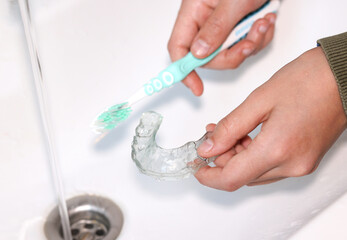 Hand cleaning transparent  retainer with toothbrush and toothpaste over sink.  - obrazy, fototapety, plakaty