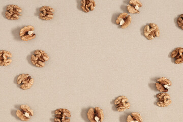 Frame made of dry walnut on beige table. Walnuts are scattered on beige background. Flat lay, top view, copy space