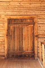 Old closed wooden door on a wooden building with metal hinges.