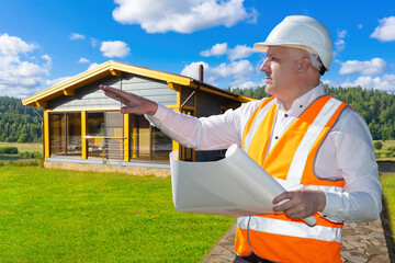 Builder man. Guy is in charge construction process. Architect in orange vest points into distance. Man stands near one-story cottage. Builder designer in helmet inspects constructed building