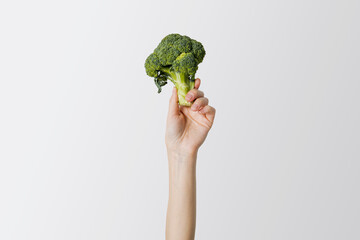 Fototapeta na wymiar Female hand raised up fresh broccoli on a white background