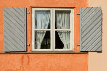 White wood framed window on a old building with grey painted exterior wood shutters.