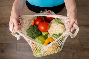 Women's hands hold a bag with fresh vegetables on the background of a wooden floor. Top view, flat lay
