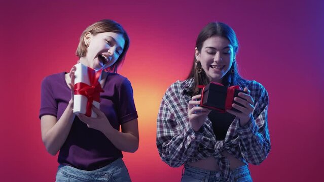 Wow present. Amazed female friends. Neon light people. Happy expressive women looking on gift boxes in hands posing blue magenta background.