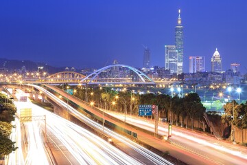 Fototapeta premium Night scenery of Taipei City with view of Taipei 101 Tower in downtown, MacArthur Bridge across river and car trails on Dike Avenue ~ Taipei cityscape at dusk by riverside (long exposure effect)