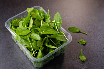 Spinach leaves in a plastic sales package, on dark background.