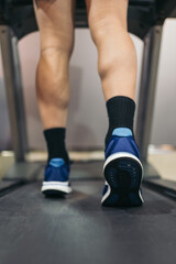 Vertical cropped close up image of young sporty man in gym exercising on treadmill.