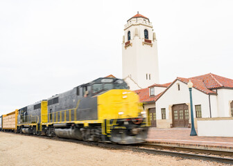 Train speeds past a depot with tall clock tower