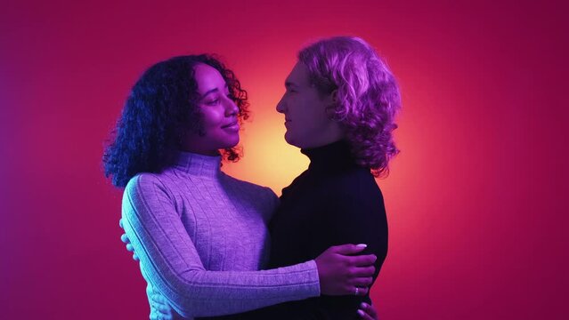 Diverse couple. Harmonic relationship. Neon light portrait. Happy man and woman hugging together on purple red background.
