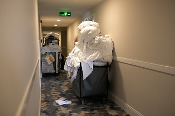 Cleaners trolley with cleaning equipments at hotel. Trolley full of dirty white sheets of guests in...