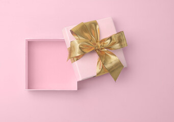 Pink empty gift box open with golden golden bow and ribbon