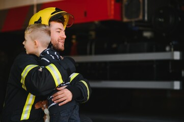 Fototapeta premium Dirty firefighter in uniform holding little saved boy standing on black background.