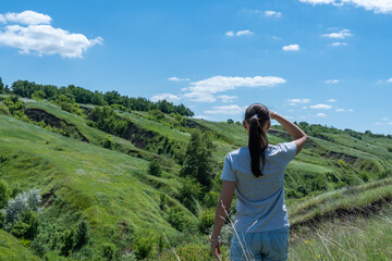 Woman looking on ravine covered with greenery. Young female traveler see landscape valley with geological faults. She admires earthen mountains and relief. Girl explore world. Positive emotion.