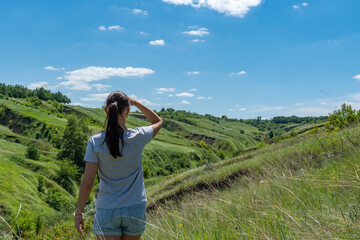 Woman looking on ravine covered with greenery. Young female traveler see landscape valley with geological faults. She admires earthen mountains and relief. Girl explore world. Positive emotion.