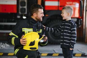 Portrait of rescued little boy with firefighter man standing near fire truck. Firefighter in fire...