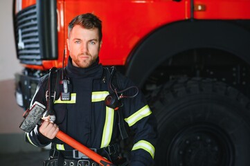 Photo of young fireman with sledgehammer in hands near fire engine