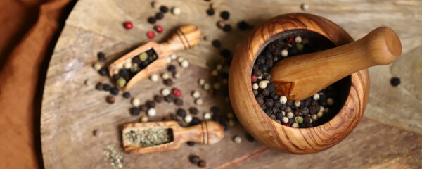 Mix of peppercorns in a wooden mortar and wooden spatulas.