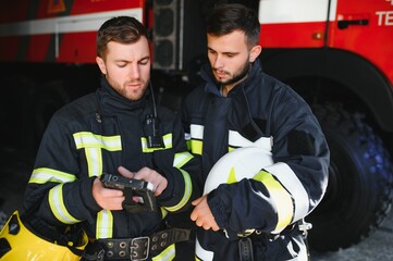 Portrait of two firefighters in fire fighting operation, fireman in protective clothing and helmet using tablet computer in action fighting