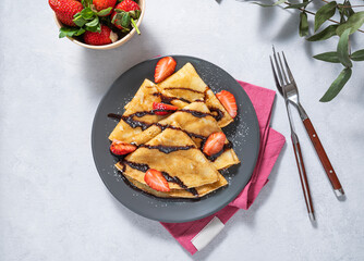 Sweet crepes with fresh strawberry and chocolate  on a gray plate on a light background. The concept of homemade healthy food.