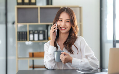 Smiling Asian businesswoman enjoying a phone call with a client in the office.