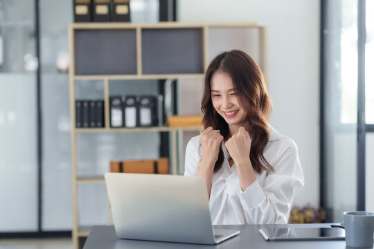 Attractive Asian businesswoman raising hands happily with successful plan with happy smile with laptop computer.