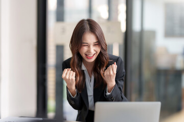 Obraz premium Attractive Asian businesswoman raising hands happily with successful plan with happy smile with laptop computer.