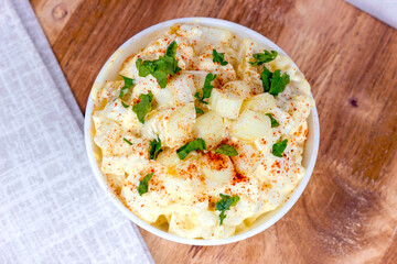 Fresh homemade traditional old-fashioned Amish Potato Salad with potatoes, boiled eggs, creamy dressing and celery in a white bowl on wooden background top view. - 568511378
