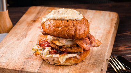 American food burger with fried chicken, bacon, pickled cucumbers, tomatoes, mustard and sauce.